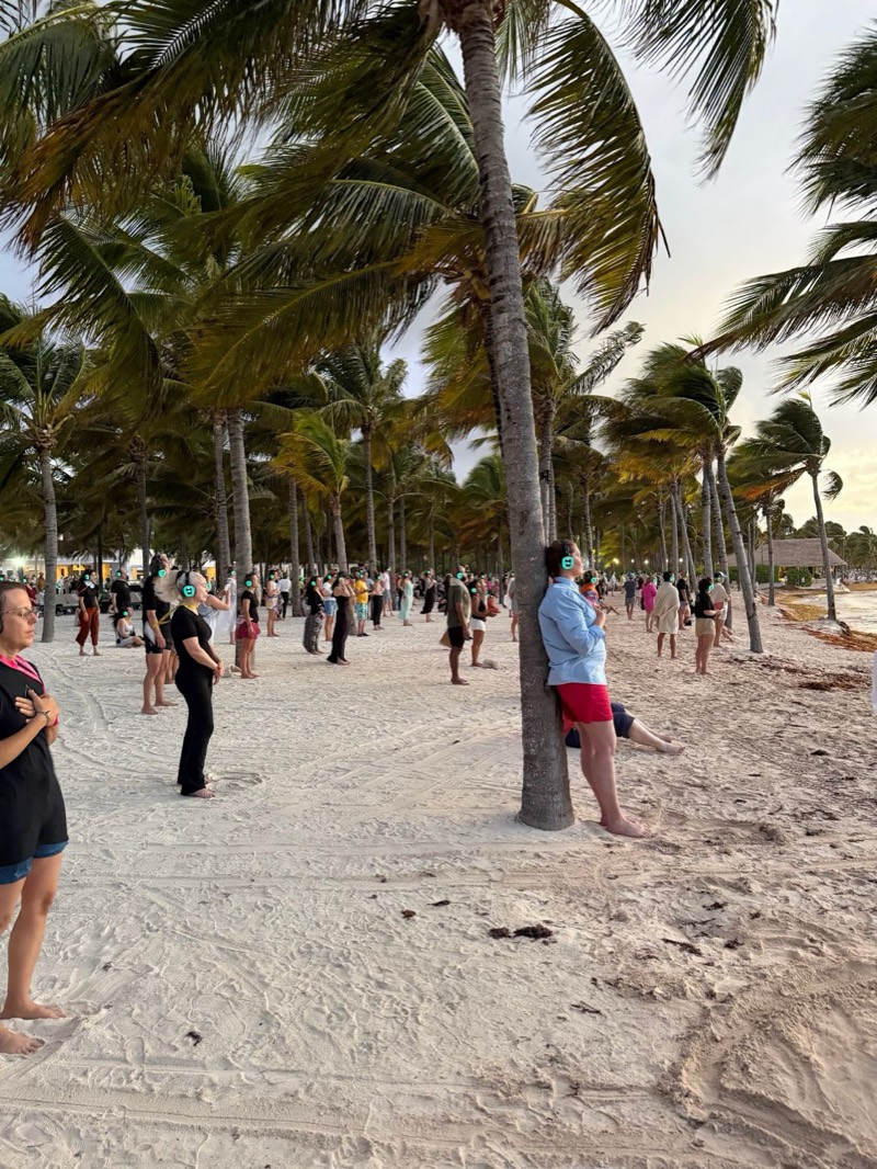 Fejhallgatós emberek a cancúni tengerparton, pálmafák alatt, hajnalban, egy élő sétálómeditáció kezdetére várva
