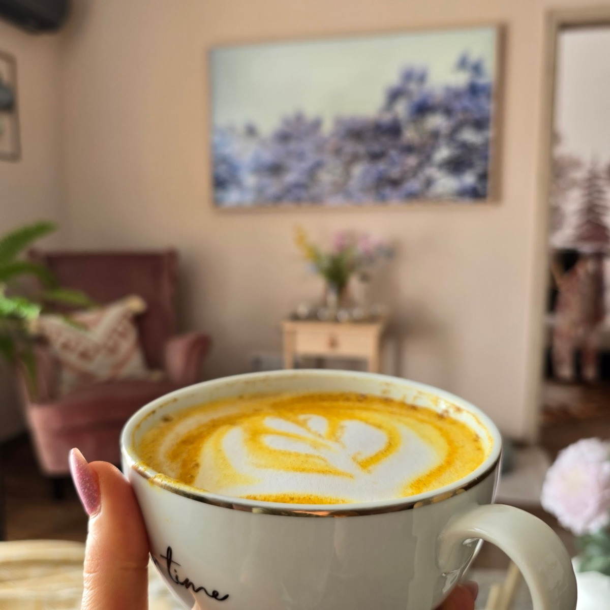 Aranysárga latte szív alakú tejhabmintával, kézben tartva